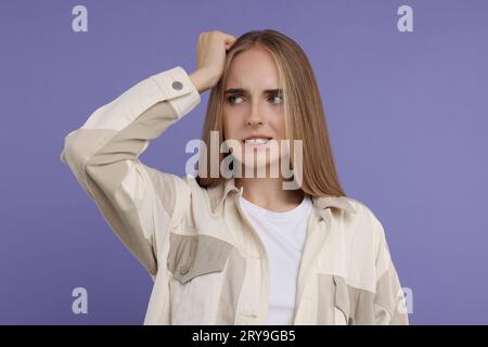 Porträt einer peinlichen jungen Frau auf violettem Hintergrund Stockfoto