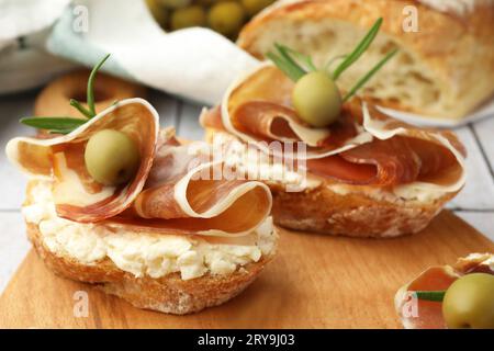 Leckere Sandwiches mit Schinken, Rosmarin und Oliven auf Holzbrett, Nahaufnahme Stockfoto