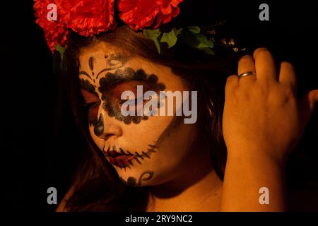 Catrina blickt nach unten und ordnet ihr Haar mit roten Blumen auf dem Kopf Stockfoto