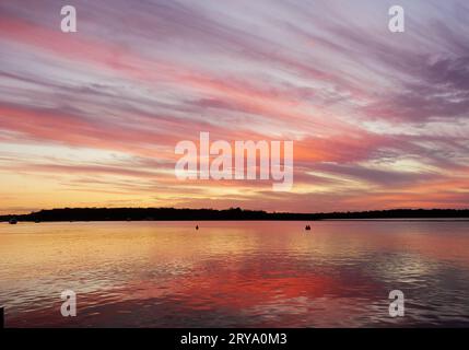 Sonnenuntergang über der Bucht in Tin Can Bay Queensland Australien. Schön, rosa und lila reflektiert auf dem Wasser. Mit einem Streifen Land am Horizont. Stockfoto