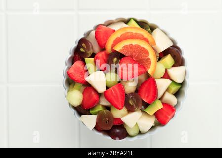 Top View frischer Obstsalat in der Schüssel, geschnittenes Obst Erdbeere, Birne, Traube, Avocado und Orange Grapefruit auf weißem Tisch Stockfoto
