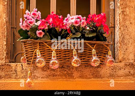 Wunderschönes Haus pflanzte rosa und rote Blumen in einem Korb an einem Fenster draußen an einem sonnigen Tag. Dekoration und Landschaftsdesign Stockfoto