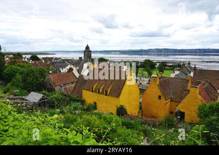 Historische Gebäude im Dorf Culross, Schottland, mit hellgelber Ockerfarbe und Dachziegeln aus Terrakotta. Der Firth of Forth liegt dahinter Stockfoto