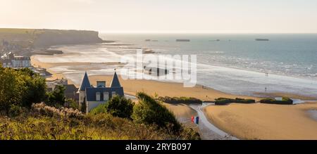 Blick auf den Strand von Arromanches in der Normandie bei Sonnenuntergang mit Überresten des Mulberry Hafens aus dem Zweiten Weltkrieg auf dem Sand und den Phoenix Caissons im Meer. Stockfoto