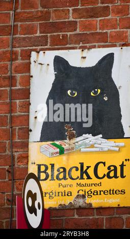 Ein farbenfrohes Vintage-Metallschild, das Black Cat Virginia Zigaretten angibt. Der Werbespot ist an einer roten Ziegelwand. Stockfoto
