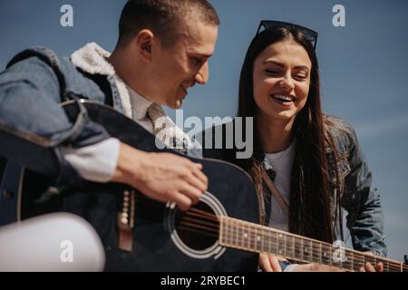 Nahaufnahme eines gutaussehenden Mannes, der vor seiner Freundin Gitarre spielt und Spaß beim Sitzen hat Stockfoto