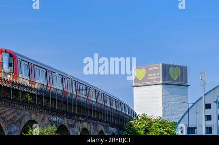 London, England - 15. Juni 2023: Ein Zug fährt in North Kensington mit dem „Forever in Our Hearts“-Unterstützungsbanner, das auf dem Grenfell-Turm im sichtbar ist Stockfoto