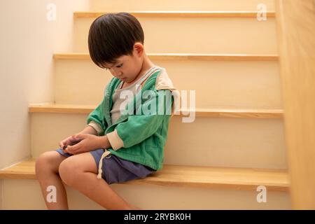 Ein Junge, der von seiner Mutter heimlich beschimpft wurde, kam, um auf der Treppe am Telefon zu spielen. Stockfoto