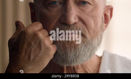 Kaukasischer alter pensionierter bärtiger Mann älterer Mann 60er Jahre Person bärtiger älterer Großvater berühren Bartmann reifes berührendes Gesicht graues Haar Hautpflegeporträt Stockfoto