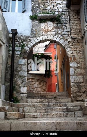 Eine schmale Straße aus Stein erhebt sich auf einem Hügel durch einen Bogengang in ein Viertel in Rovinj, Kroatien. Stockfoto