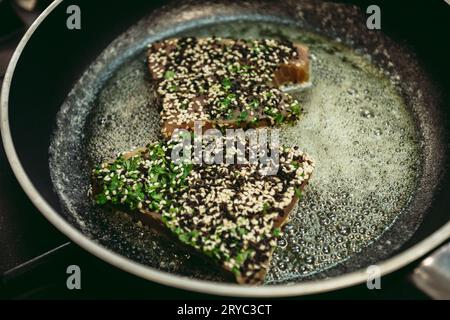 Frische rohe Thunfischsteaks mit Pfeffer und anderen Zutaten, die zum Kochen zubereitet werden. Gebratener Thunfisch in der Pfanne auf dunklem Backgorund. Stockfoto