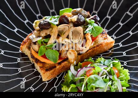 Pilze auf Toast mit Hummus, Knoblauchbutter, Thymian und Trüffelöl auf Holztisch mit Gabel, Messer und Limonadengetränk Stockfoto