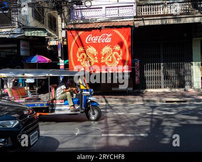 Ein traditionelles Tuk-Tuk-Fahren vor einem prominenten Coca-Cola-Schild in Bangkok, Thailand. Stockfoto