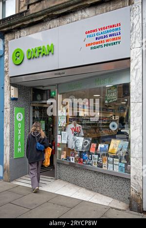 Junge Frau, die in einen Oxfam Music Shop in Stockbridge, Edinburgh, Schottland, Großbritannien geht. Stockfoto