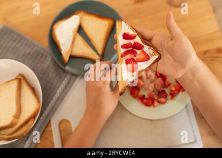 Von oben, eine Frau, die Frischkäse Toast mit Erdbeeren für einen Snack zubereitet Stockfoto
