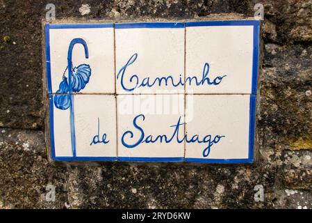 Ein Schild aus blauen Kacheln mit dem Symbol eines Pilgerstabs und einer Muschel, das an einer Wand entlang des portugiesischen Jakobsweges, dem portugiesischen Weg des Heiligen, zu sehen ist James in der Nähe von Valenca. Stockfoto