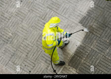 Draufsicht eines Arbeiters, der den Bürgersteig mit einem Hochdruckwasserstrahl reinigt Stockfoto