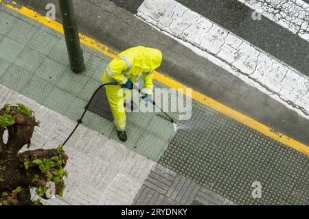 Draufsicht eines Arbeiters, der den Bürgersteig mit einem Hochdruckwasserstrahl reinigt Stockfoto