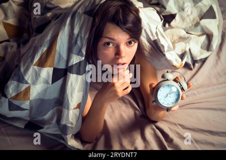Das Mädchen schläft, versteckt sich unter einer Decke mit einem Wecker. Stockfoto