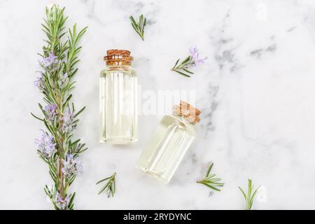 Ätherisches Rosmarinöl in Glasflasche und Zweige auf Marmortisch Stockfoto
