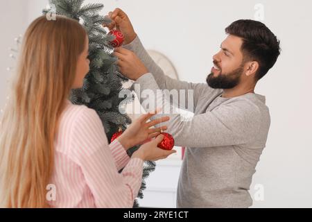 Glücklicher junger Mann mit seiner Frau, die zu Hause den Weihnachtsbaum schmückt Stockfoto