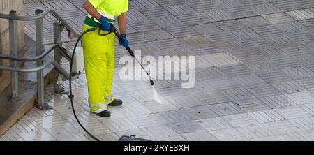 Arbeiter, der einen Bürgersteig mit einem Hochdruckwasserstrahl reinigt Stockfoto