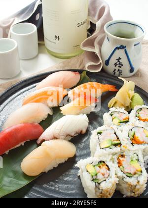 Farbenfrohe Auswahl an Nigiri-Sushi auf Teller mit kalifornischen Brötchen, serviert mit Sake, im japanischen Restaurant. Stockfoto