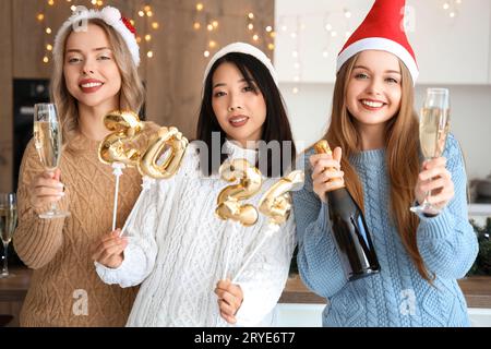 Junge Frauen mit Champagner und Figur 2024 feiern Weihnachten in der Küche Stockfoto