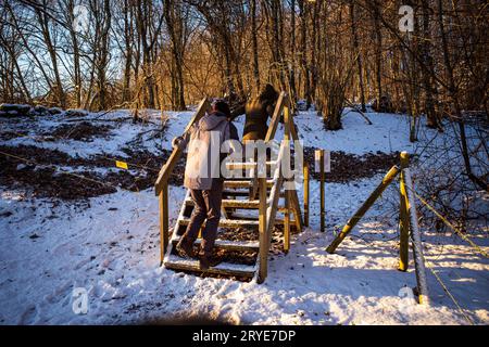Ein Paar, das in einer schneebedeckten Winterlandschaft über Holzstufen schlendert und sich im warmen Sonnenlicht sonnt. Stockfoto