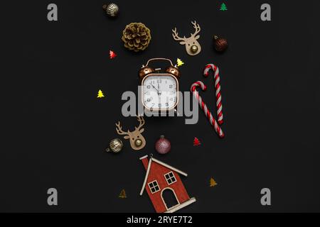 Wecker mit Weihnachtsdekoration und Zuckerstangen auf schwarzem Hintergrund Stockfoto