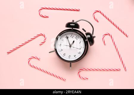 Wecker mit weihnachtlichen Zuckerstangen auf rosafarbenem Hintergrund Stockfoto
