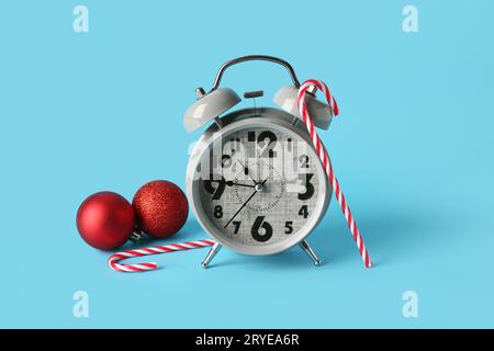 Wecker mit Weihnachtskugeln und Zuckerstangen auf blauem Hintergrund Stockfoto
