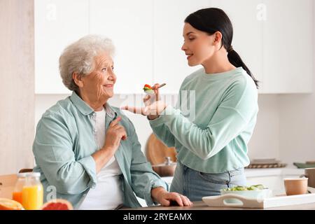 Ältere Frau mit ihrer Tochter, die Gemüsesalat in der Küche isst Stockfoto