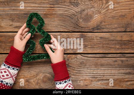 Weibliche Hände mit Dekoration in Form eines Weihnachtsbaums auf hölzernem Hintergrund, Nahaufnahme Stockfoto