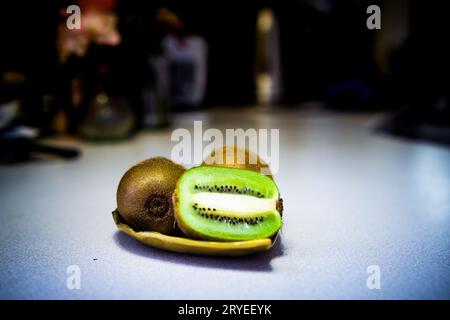 Drei Kiwi-Früchte, eines in zwei Hälften auf goldenem Metallblattblech in einer nicht fokussierten Küche Stockfoto