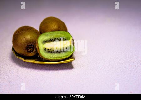 Drei Kiwi-Früchte, eines in zwei Hälften auf goldenem Metallblatt isoliert Stockfoto