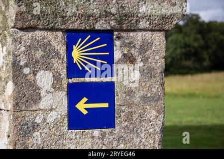 Jakobsweg Gelbes Jakobsmuschel- und Pfeilschild an der alten Steinmauer Stockfoto