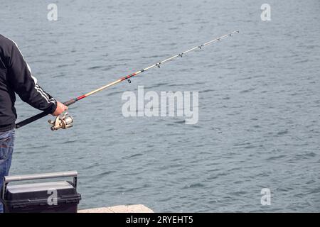 Fischer, der am Rande des Docks mit Angelrute in der Nähe des Meeres steht Stockfoto