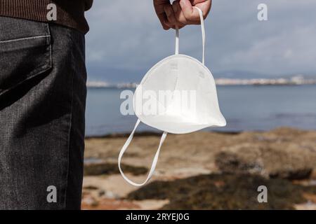 Männliche Hand hält eine Gesichtsmaske an einem wilden Strand an einem sonnigen Tag Stockfoto