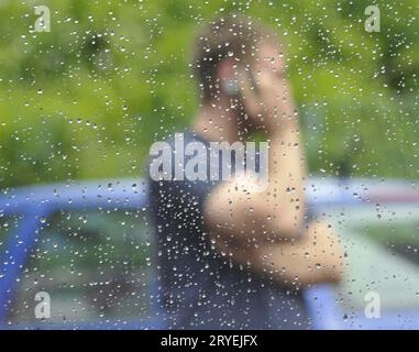Regen fällt auf ein Fenster und eine Person Stockfoto
