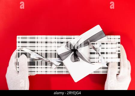 Weiße Hände mit Handschuhen, die ein Weihnachtsgeschenk auf rotem Hintergrund halten Stockfoto