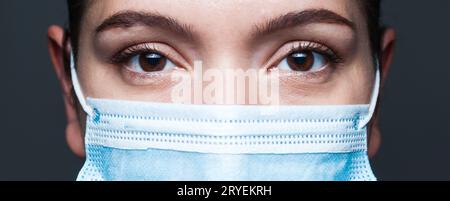 Junge kaukasische Frau trägt blaue chirurgische Gesichtsmaske Nahaufnahme Breitbild-Porträt Stockfoto