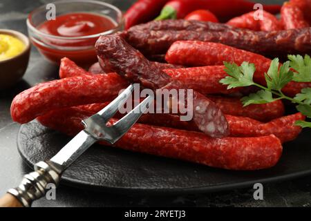 Dünne, trocken geräucherte Würstchen und Gabel auf dunklem Tisch, Nahaufnahme Stockfoto