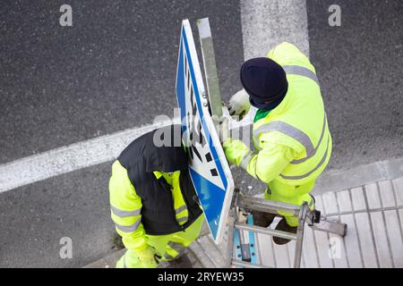 Arbeiter tauschen ein beschädigtes Straßenschild auf dem Bürgersteig aus Stockfoto