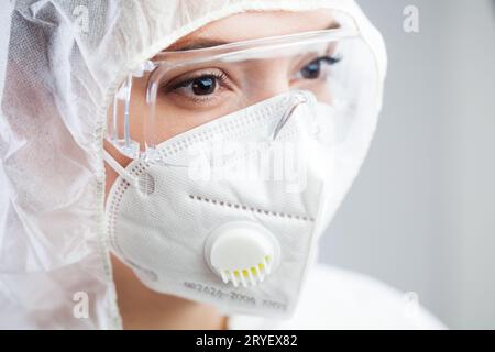 Großaufnahme von müden weiblichen Doktor, Krankenschwester oder Labortechniker tragen PSA Schutzanzug, weiße Gesichtsmaske und Schutzbrille Stockfoto