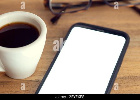 Smartphone am Schreibtisch mit weißem Bildschirm, Brille und Tasse Kaffee auf Holztisch. Mustervorlage Stockfoto