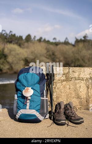 Rucksack mit Muschelsymbol des Jakobsweges, Wanderstiefeln und Stangen, die an einer Steinmauer befestigt sind. Pilgerfahrt nach Santiago de C. Stockfoto