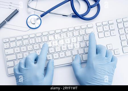 Der Arzt hält Handschuhe, die auf der Computertastatur tippen. Telemedizinische oder medizintechnische Konzepthintergründe. Draufsicht Stockfoto