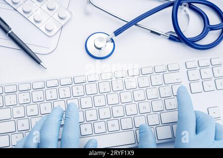 Der Arzt hält Handschuhe, die auf der Computertastatur tippen. Telemedizinische oder medizintechnische Konzepthintergründe. Draufsicht Stockfoto