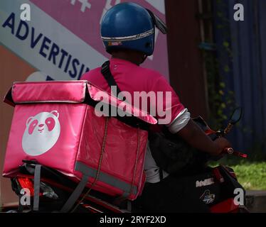Das Foodpanda-Logo ist auf der Behältertasche auf der Rückseite des Motorrads aufgedruckt. Der Fahrer ist unterwegs und liefert eine Lieferung. Stockfoto